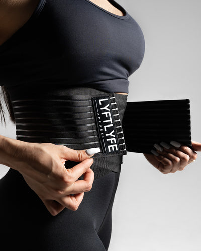 Female model tightening black LYFTLYFE compression belt at waist.
