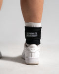 Rear view of ankle strap secured on white sneaker, showcasing Dominate Adversity logo.