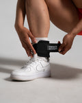 Close-up of athlete fastening LYFTLYFE cable ankle strap in black with strong velcro around white sneaker.