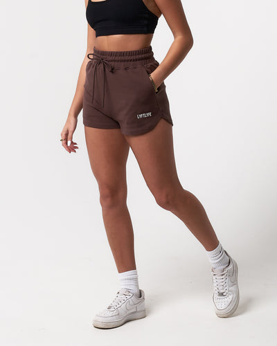 Front view of women’s high-waisted dark brown Balance Shorts featuring an elasticized waistband, drawstring, and side pockets.