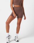 Woman wearing brown LYFTLYFE 4-inch shorts, styled with minimal seams and smooth compression.