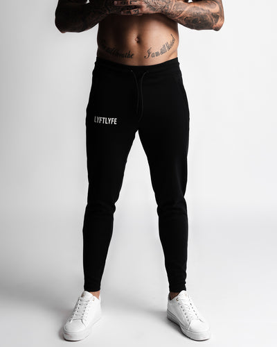 Men’s black joggers left side view showing zipper pocket and slim leg fit.
