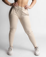 Woman wearing beige joggers, standing pose showing full tapered fit. 