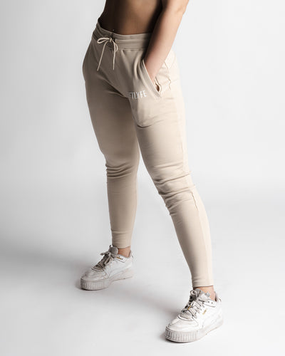 Woman wearing beige joggers, standing pose showing full tapered fit. 