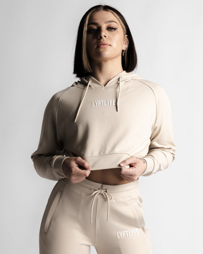 Cropped front view of LYFTLYFE React hoodie in beige showing logo and high-waist jogger pairing.