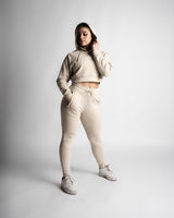 Woman wearing beige cropped hoodie and matching joggers, standing pose showing full tapered fit.