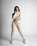 Woman wearing beige cropped hoodie and matching joggers, standing pose showing full tapered fit.