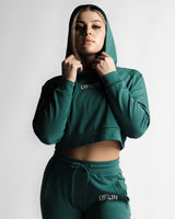 Woman modeling hooded LYFTLYFE crop hoodie in green with confident look.