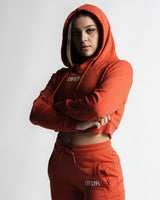 Woman in side pose wearing red React crop hoodie with hood on and high-rise joggers. 