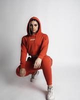 Woman wearing red LYFTLYFE joggers and cropped hoodie in crouched side profile.