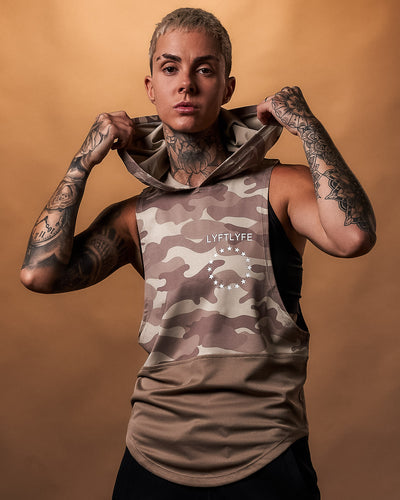 Light brown camouflage sleeveless hoodie with a white brand logo on a light gray background