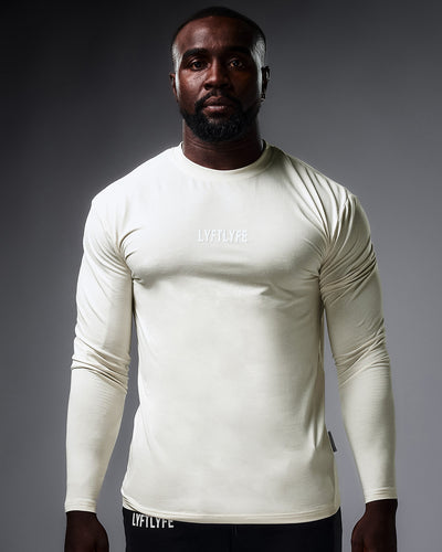 Men’s LYFTLYFE essential long sleeve shirt in offwhite with white chest logo on light grey background.