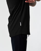 Close-up of the Dominate Adversity flag tag on the black Contour Men’s T-Shirt, stitched on the lower side seam for brand detailing.