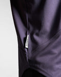 Detailed shot of Dominate Adversity tag stitched into the curved hem of the lightweight performance tank in purple. 