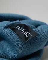 Detail of black LYFTLYFE fabric tag stitched inside blue beanie.