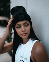 Female model wearing black LYFTLYFE beanie with rubberized logo and white gym top.