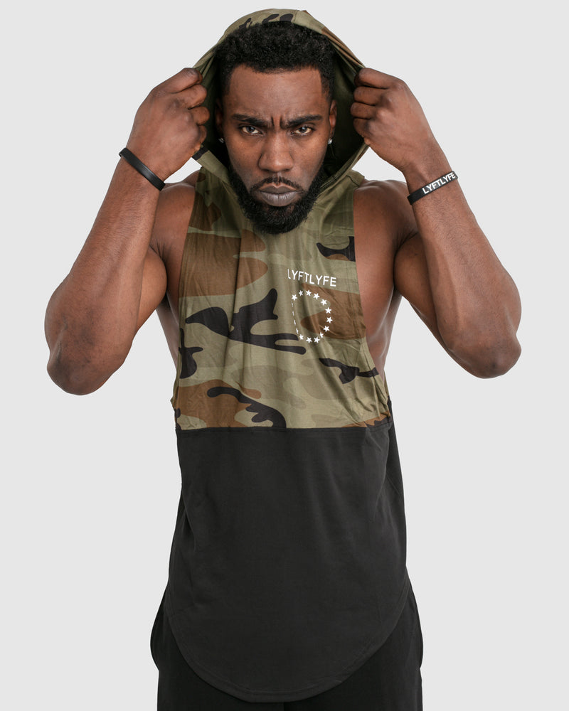 Mens sleeveless hoodie made with two panels. The top panel is camo, including the hood. The bottom panel is black. 